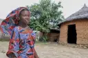 Młoda kobieta w kolorowym stroju stoi przed glinianymi chatami w Togo.