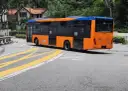 Pomarańczowo-niebieski autobus miejski na zakręcie drogi z żółtymi pasami.