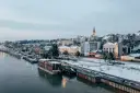 Widok na zimowe miasto nad rzeką z łodziami i ośnieżonymi budynkami.