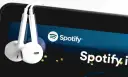 Białe słuchawki wiszą na ekranie smartfona z logo Spotify.