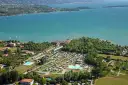 Widok z lotu ptaka na camping Baia Verde nad turkusowym jeziorem, z basenami i licznymi namiotami.