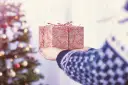 Ręce trzymające świąteczny prezent owinięty w papier z wzorem gałązek i śnieżynek.