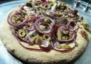 Pizza z anszua, oliwkami i czerwoną cebulą, gotowa do pieczenia.