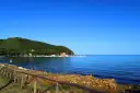 A tranquil bay in Tuscany with sailboats docked, a green hillside, and a rustic wooden fence in the foreground.