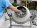Mieszanie betonu w betoniarce. Pracownik w rękawicach sprawdza konsystencję, zastanawiając się, ile cementu na metr sześcienny betonu potrzeba do uzyskania idealnej mieszanki.