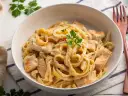 Kremowe fettuccine z kurczakiem, idealne do przygotowania według przepisu Fettuccine Alfredo. Danie ozdobione natką pietruszki.