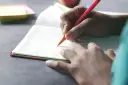 Dłoń pisze w zeszycie, co to dysgrafia? Trudności z pisaniem mogą dotyczyć każdego.