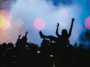Tłum na jednym z największych festiwali muzycznych na świecie. Kobieta na rękach, ręce w górze, światła sceny.