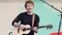 Ed Sheeran gra na gitarze akustycznej na tle pofalowanej, kolorowej kurtyny.