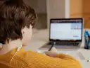 Chłopiec w żółtym swetrze uczy się zdalnie, pisząc notatki. Czy uczniowie dostaną laptopy, by móc tak pracować?