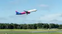Samolot Wizz Air wznoszący się na tle błękitnego nieba z chmurami.