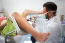 Lekarz w masce i rękawiczkach aplikuje octenisept na krocze po porodzie.
