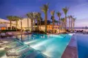 Luxury resort pool with palm trees and lounge chairs at dusk.