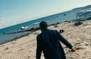 Mężczyzna w garniturze idzie po plaży usianej szczątkami samolotu. Chce zostawić świat za sobą, szukając ratunku.