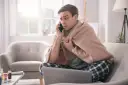 Chory mężczyzna owinięty kocem rozmawia przez telefon, martwiąc się, czy sobota i niedziela wlicza się do chorobowego.