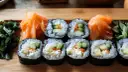Gotowy sushi przepis na talerzu: rolki z ryżem, ogórkiem i łososiem, podane z marynowanym imbirem i zielonymi dodatkami.