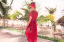 Kobieta w zwiewnej, **czerwonej sukience boho** w białe grochy, z czerwoną opaską na głowie, pozuje na tle palmy i plaży.