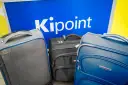 Three suitcases in front of a blue sign with "Kipoint" in white letters.