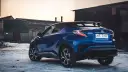 Niebieska Toyota C-HR Hybrid na tle opuszczonych budynków. Czy wybrać hybrydę czy benzynę?