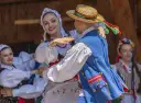 Uśmiechnięta para w tradycyjnych strojach tańczy do skocznych piosenek ludowych.