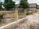 Budowa fundamentu pod ogrodzenie: betonowy murek, drewniane słupki i piasek.