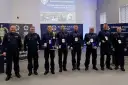 Policjanci w mundurach stoją w rzędzie, niektórzy trzymają nagrody i dyplomy.