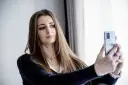 Młoda kobieta robi sobie selfie telefonem, przygotowując się do zrobienia zdjęcia do CV.