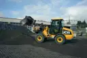 Żółta ładowarka JCB 406 z podniesioną łyżką, gotowa do pracy. Dane techniczne tej maszyny pozwalają na efektywne przenoszenie materiałów.