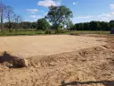 Przygotowanie terenu pod budowę: wyrównana piaszczysta działka z zaznaczonymi granicami, otoczona drzewami.