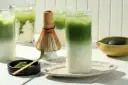 Zielone napoje matcha z lodem, bambusowa miotełka i proszek matcha.