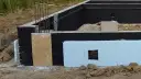 Fundament z czarną izolacją przeciwwilgociową i płytami XPS. Widać zbrojenie i fragmenty szalunku. Dobra jaka izolacja na fundament.