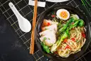 Miseczka ramenu z plastrami wieprzowiny, jajkiem na twardo, warzywami i makaronem. Dodatki do ramenu, takie jak szczypiorek i sezam, podkreślają smak.