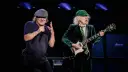 Brian Johnson i Angus Young, legendarny skład AC/DC, na scenie. Brian śpiewa do mikrofonu, Angus gra na gitarze.