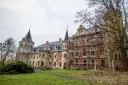 Pałac w Krowiarkach, majestatyczna budowla z wieżami i ceglaną fasadą, otoczony jesienną zielenią, częściowo w rusztowaniach.