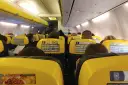 Widok z wnętrza samolotu Ryanair z żółtymi siedzeniami i pasażerami.