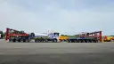 Ciężarówka z naczepą tandem przewozi element turbiny wiatrowej. Obok stoi inna naczepa z dźwigiem.