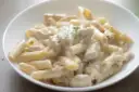 Penne w kremowym sosie serowym z kawałkami kurczaka, udekorowane gałązką ziół. Pyszny makaron serowy z kurczakiem.