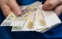 Dłonie trzymają stos banknotów 200 zł. To symbol oszczędności Polaków, które budują bezpieczeństwo finansowe.