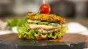 Burger z warzywną bułką, kotletem, ogórkiem, sosem i pomidorkiem na wykałaczce.