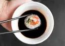 Pałeczkami zanurzam rolkę sushi w ciemnym sosie. Idealny sos słodki do sushi podkreśla smak ryby i ryżu.