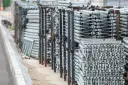 Stosy aluminiowych elementów rusztowania stojące na placu budowy.