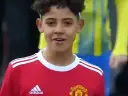 Młody piłkarz w czerwonej koszulce Manchester United, przypominający syna Cristiano Ronaldo. Jego wiek sugeruje, że to początki kariery.