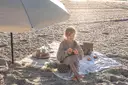 Dziewczynka na plaży pod parasolem, jedząca owoce. Idealny zestaw na wakacje nad morze z dzieckiem: koc, owoce, ananas.
