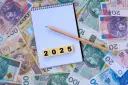Notatnik z ołówkiem i kafelkami z cyframi "2025" na tle polskich banknotów.