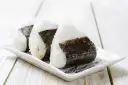 Trzy ryżowe kulki onigiri z nori na białym talerzyku. Idealne na szybki lunch, oto prosty onigiri przepis.