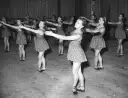 Młode tancerki w ludowych strojach ćwiczą choreografię. Ich ruchy synchronizują się z rytmem, jakby grały zespoły polskiej muzyki ludowej.