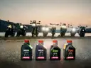 Cztery butelki oleju Motul do motocykla: NGEN5, NGEN7, 5100 i 7100, stoją na drodze o zachodzie słońca, za nimi widać rzędem motocykle.