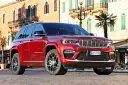 Czerwony Jeep Grand Cherokee zaparkowany na brukowanej ulicy przed budynkami z balkonami.