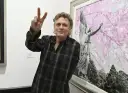 Rick Allen, perkusista Def Leppard, pozuje z uniesionym znakiem pokoju obok obrazu z aniołem i kwitnącymi drzewami.