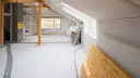 Wnętrze domu w trakcie budowy, widoczne materiały budowlane, instalacje i rusztowanie.